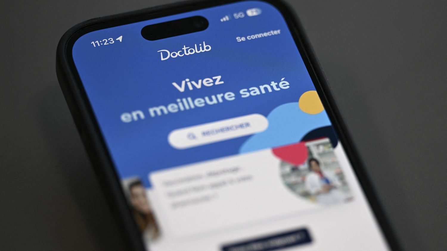 Un smartphone affiche la page d'accueil bleue de Doctolib.